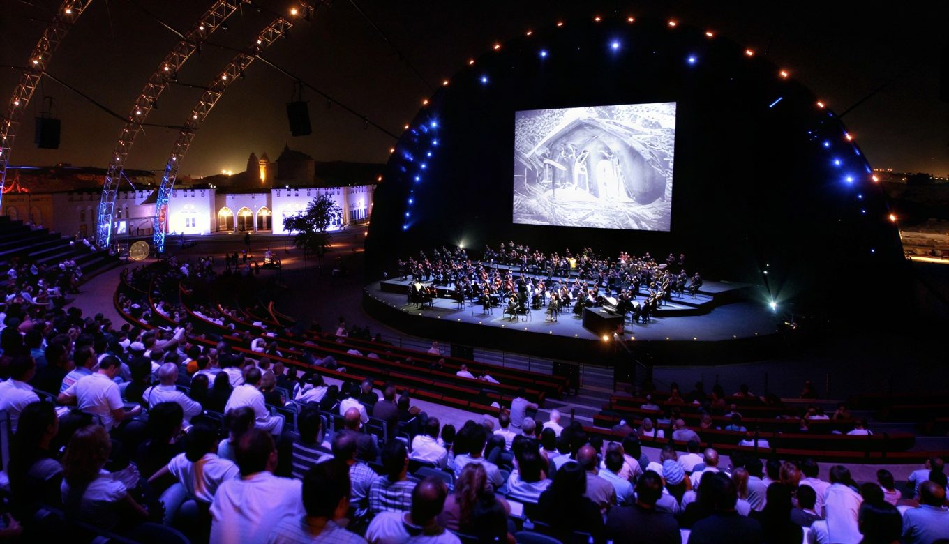 live-orchestra-film-soundtrack-screening Orchestra performing a live film soundtrack on a domed stage to a seated amphitheatre audience