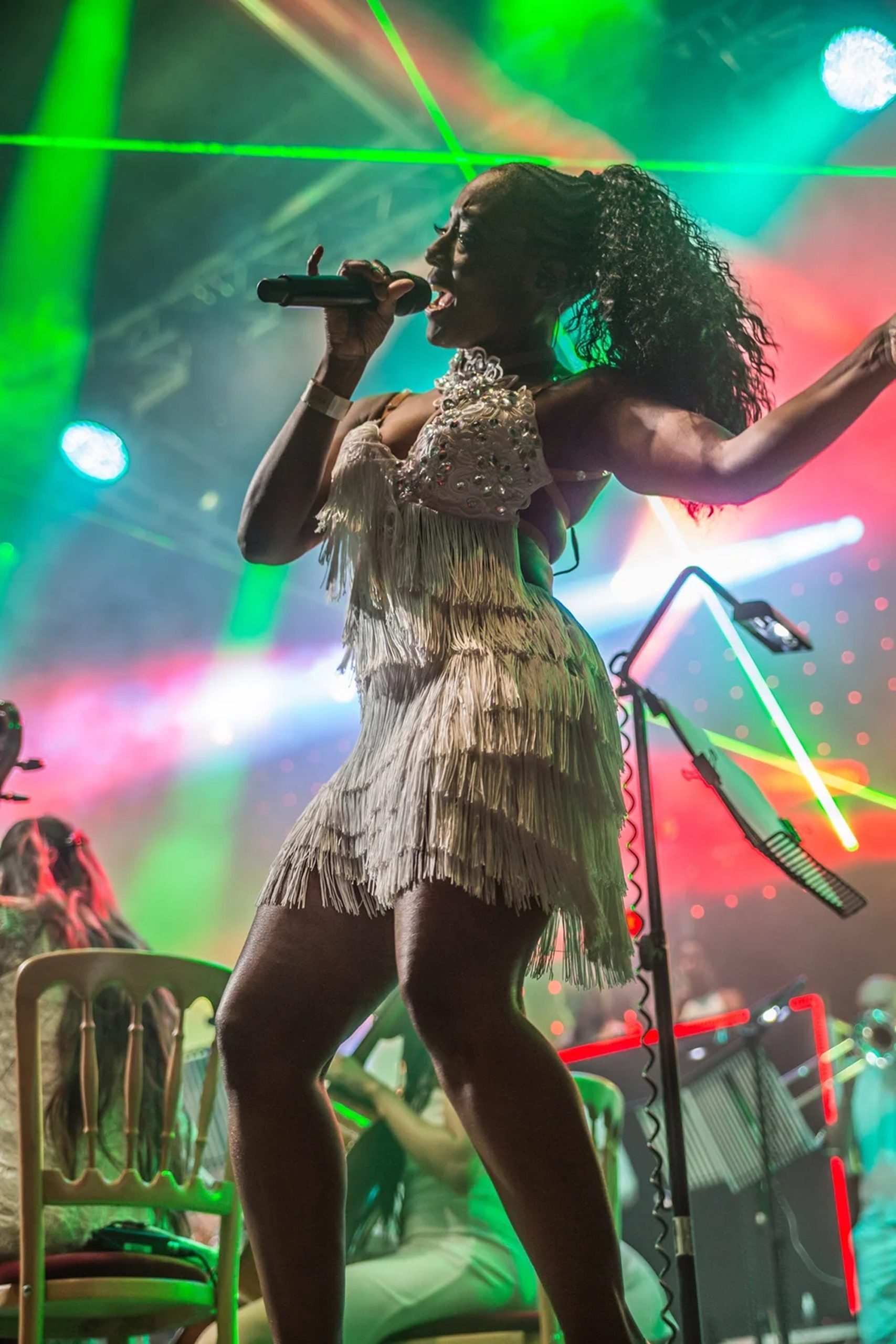 Orchestral Dance Anthems — Lead Vocalist with Laser Show Urban Soul Orchestra lead vocalist singing on stage in a white fringed dress, lit by green and red lasers.