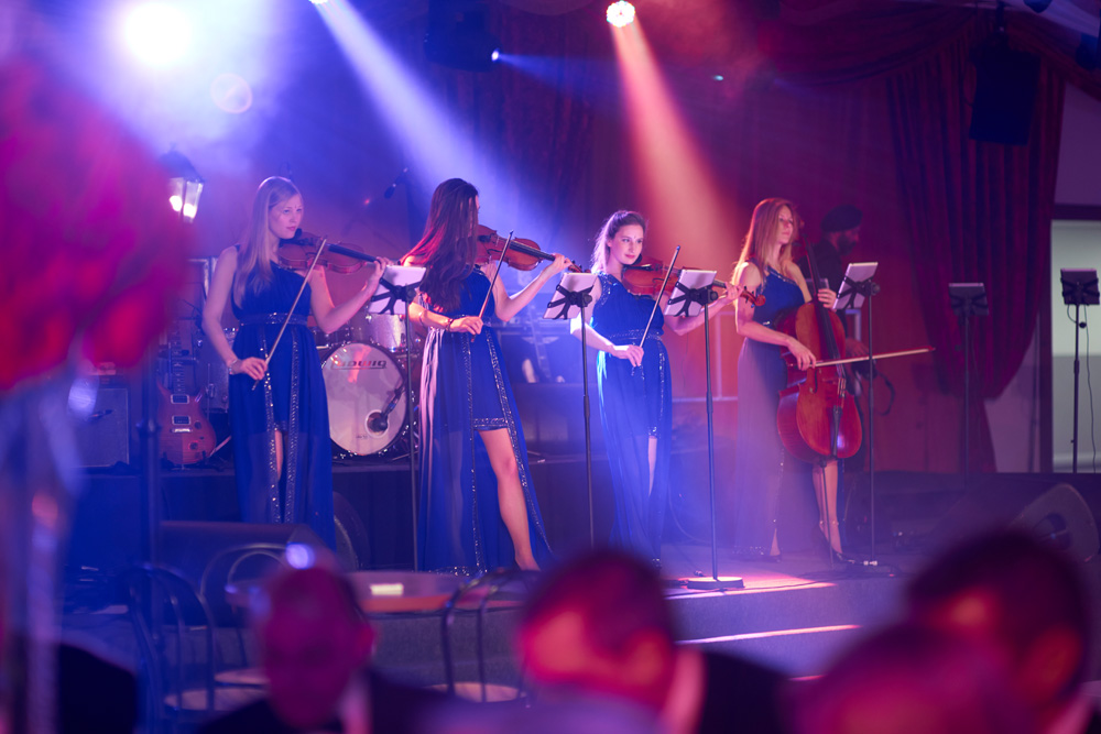 Themed Bands — Bollywood String Quartet, Stage View Four Urban Soul Orchestra string players in blue gowns performing on a lit stage, viewed across floral table arrangements.