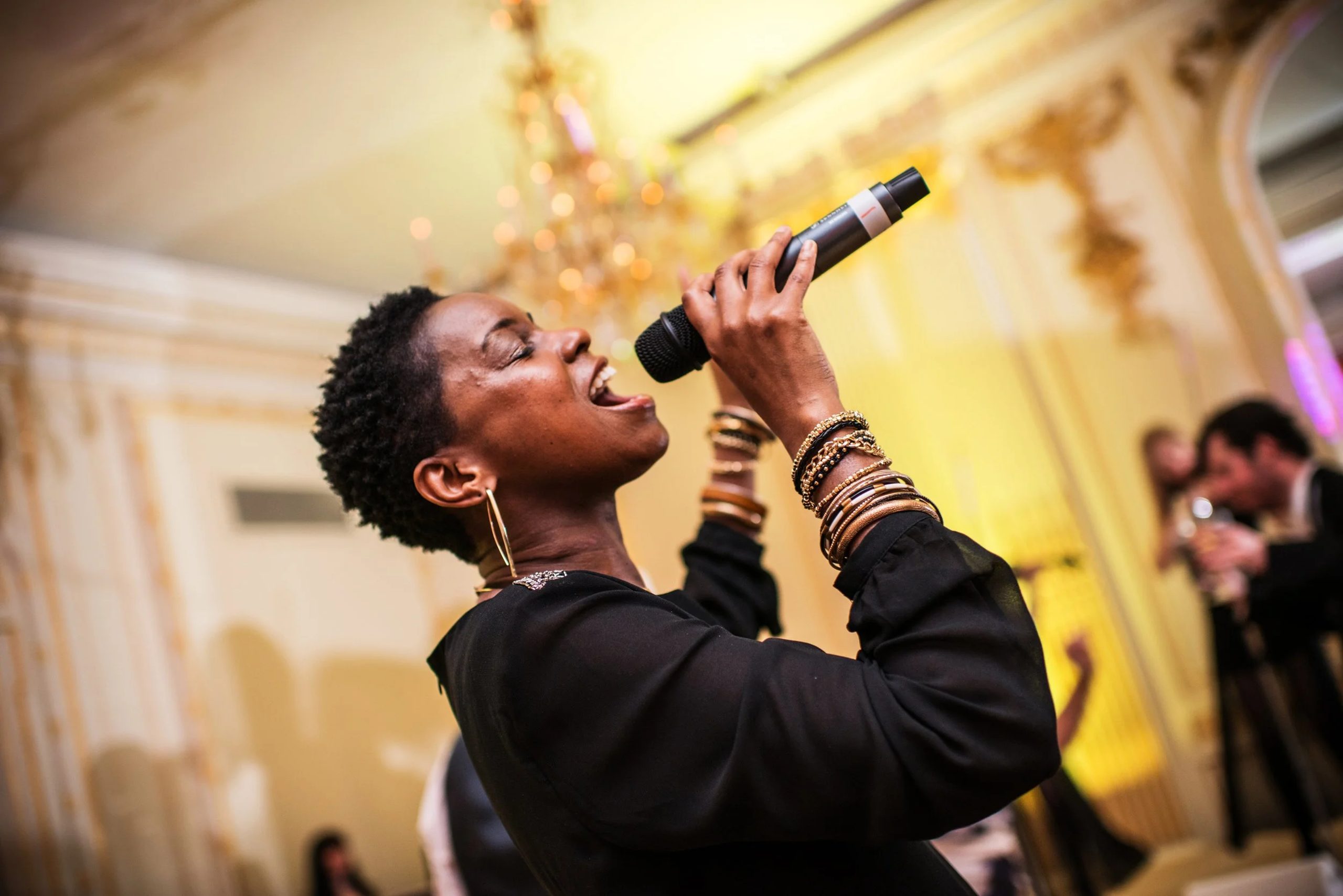 USO Lead vocalist Show Band Urban Soul Orchestra vocalist singing into a handheld microphone beneath a chandelier in a gilded ballroom