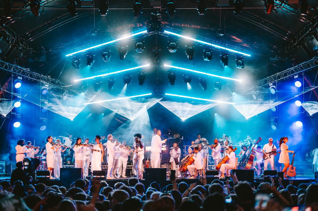 Large Orchestral Ensemble Festival Performance Urban Soul Orchestra performing a 30+ piece ensemble in white on a large festival stage with blue LED lighting and moving lights.